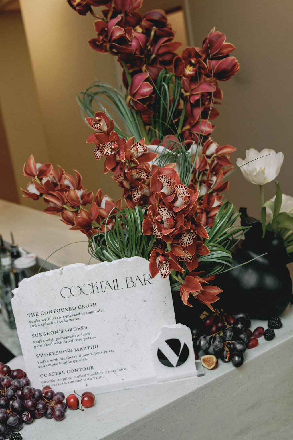 Custom cocktail bar menu with dramatic orchid floral arrangement and branded event styling at a Virginia Beach corporate grand opening designed by Lustre Theory.